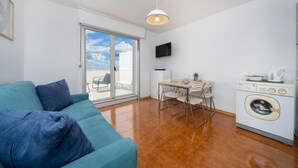 Ein modernes Wohnzimmer mit einer Couch, einem Esstisch mit Stühlen, einer Waschmaschine und einem Fernseher an der Wand.