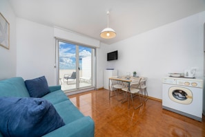 A modern living room with a sofa, a dining table with chairs, a washing machine, and a TV on the wall. - A comfortable 53-square-meter apartment, perfect for four people, located on the third floor (Scala A) of a building with an elevator (NOT suitable for people with disabilities) directly facing the seafront.The property is located in Lignano Sabbiadoro i (Lignano Sabbiadoro)