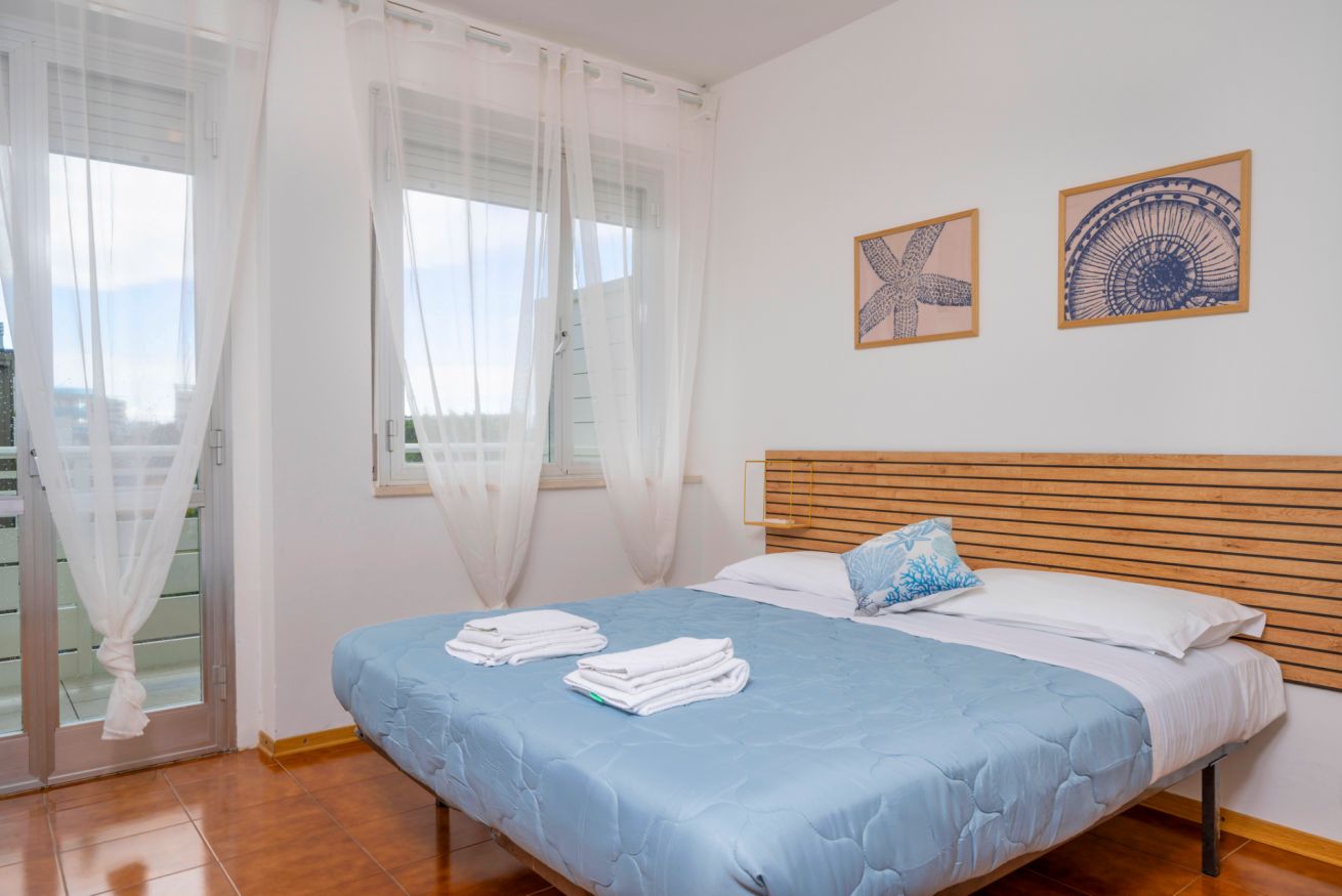A bedroom with a bed, white curtains, a wooden headboard, and two wall art pieces.