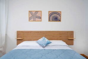 A bed with a blue quilt, a wooden headboard, and two framed wall art pieces. - A comfortable 53-square-meter apartment, perfect for four people, located on the third floor (Scala A) of a building with an elevator (NOT suitable for people with disabilities) directly facing the seafront.The property is located in Lignano Sabbiadoro i (Lignano Sabbiadoro)