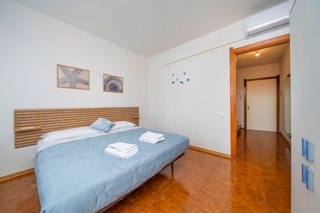 Een slaapkamer met een bed, een houten hoofdbord, een wandairconditioner en een deur die naar een andere kamer leidt.