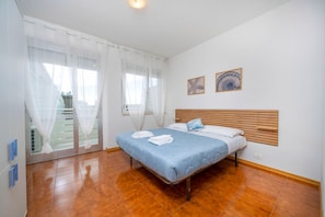 A bedroom with a bed, white curtains, a wooden headboard, and two wall-mounted pictures. - A comfortable 53-square-meter apartment, perfect for four people, located on the third floor (Scala A) of a building with an elevator (NOT suitable for people with disabilities) directly facing the seafront.The property is located in Lignano Sabbiadoro i (Lignano Sabbiadoro)