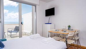 Ein Hotelzimmer mit Bett, Fernseher, Esstisch mit Stühlen und Meerblick durch eine Schiebetür.
