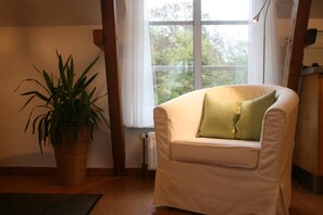 Una poltrona bianca con un cuscino verde, una pianta in vaso e una finestra con vista sugli alberi.