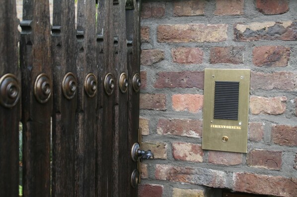 Une porte en bois avec une plaque en laiton portant l’inscription « FERIENWOHNUNG » est fixée à un mur de briques.