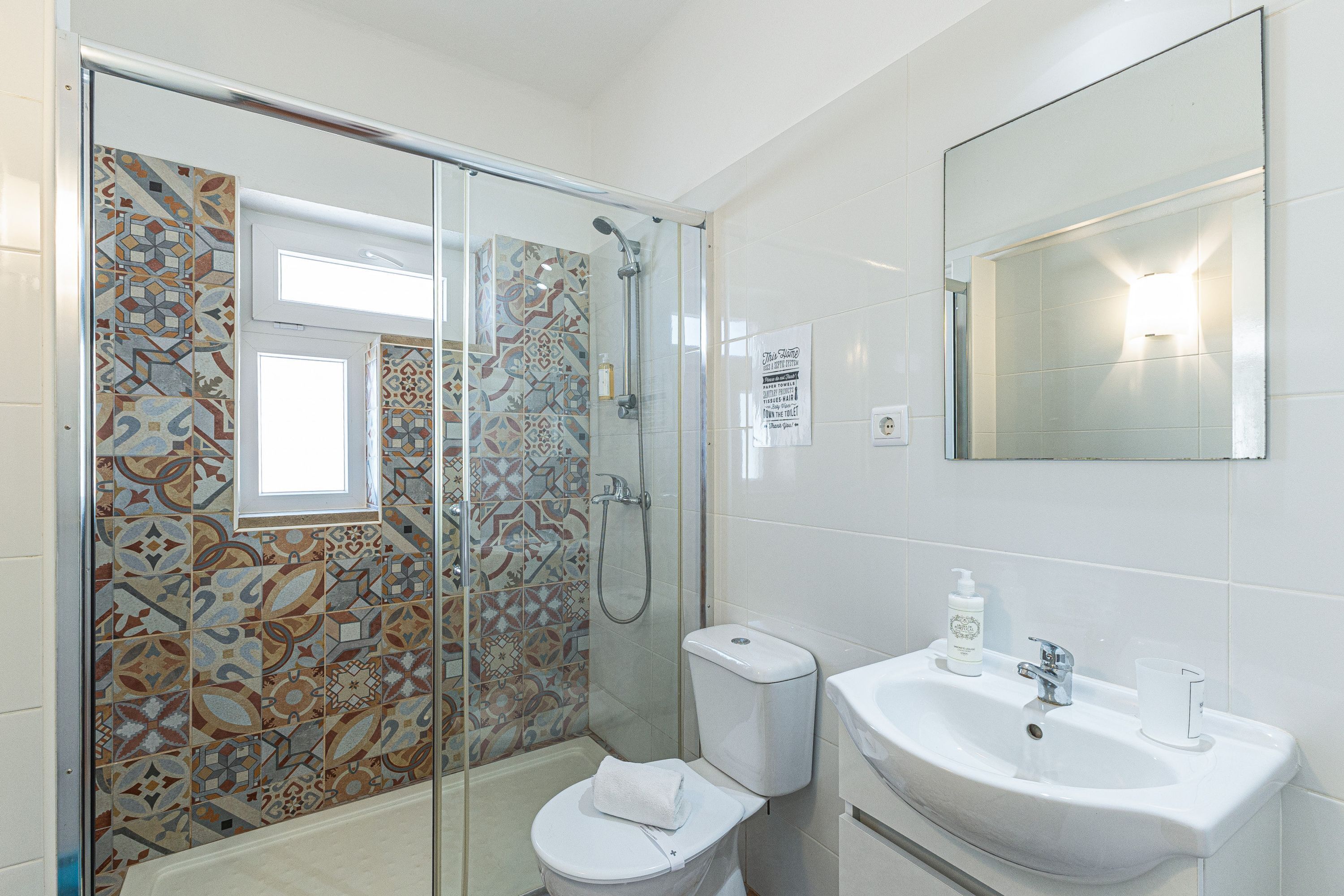 A bathroom with a shower, toilet, sink, and a mirror.