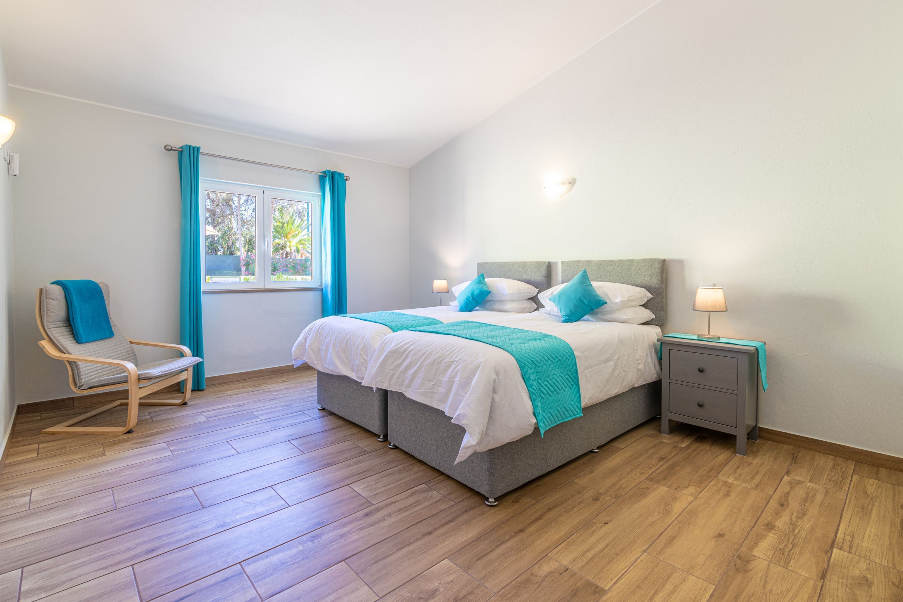 Un dormitorio con cama, mesita de noche, silla y ventana con cortinas.