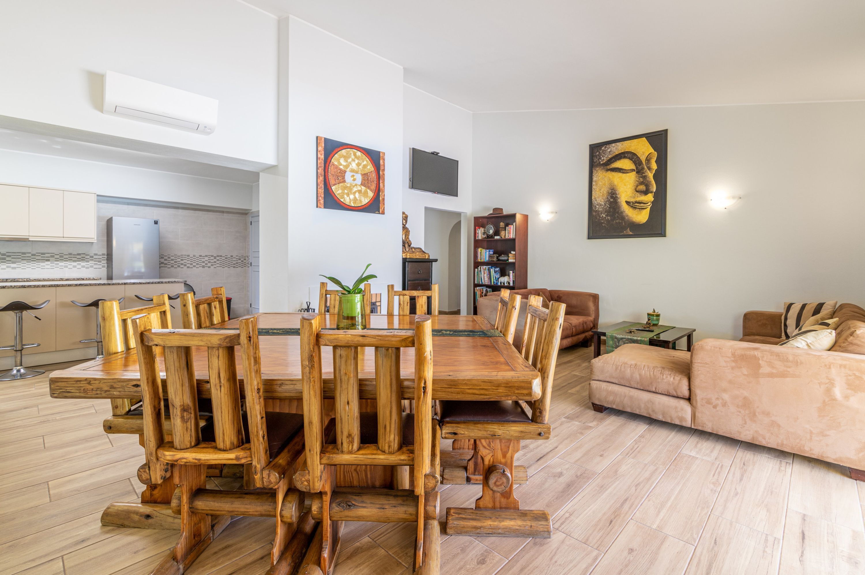 Un amplio salón con una mesa de comedor de madera, un sofá y un televisor montado en la pared.