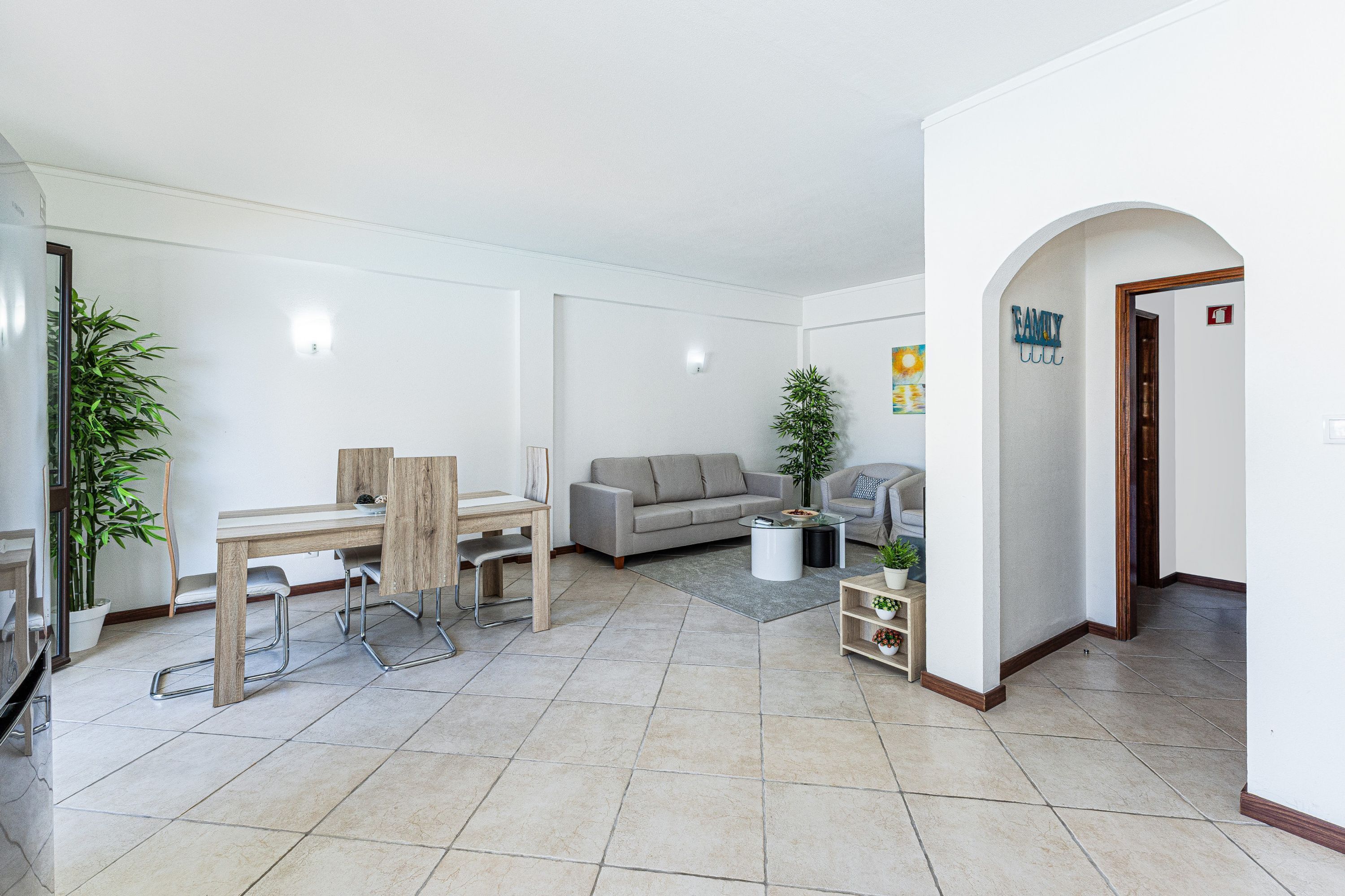 Una sala de estar moderna con comedor, un sofá gris y una pequeña mesa con una planta.