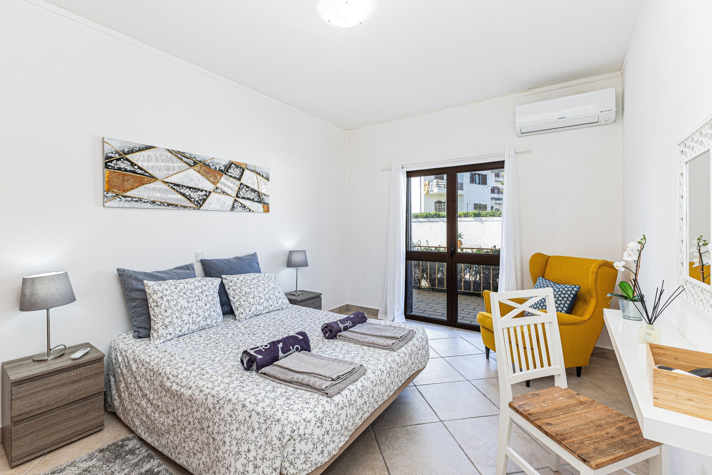 Un dormitorio con cama, mesitas de noche, un escritorio, una silla y una puerta al balcón.