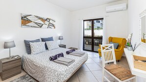 Quarto com cama, mesas de cabeceira, escrivaninha, cadeira e porta para varanda.