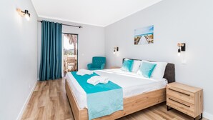 Ein Schlafzimmer mit einem Bett, einem Nachttisch, einem Stuhl, einem Fenster mit Vorhängen und einem Wandbild.
