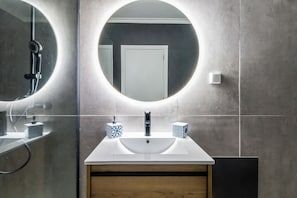 A bathroom with a round mirror, a white sink, and two patterned soap dispensers. - Portim o Resort Private Parking Pool (Portimão)