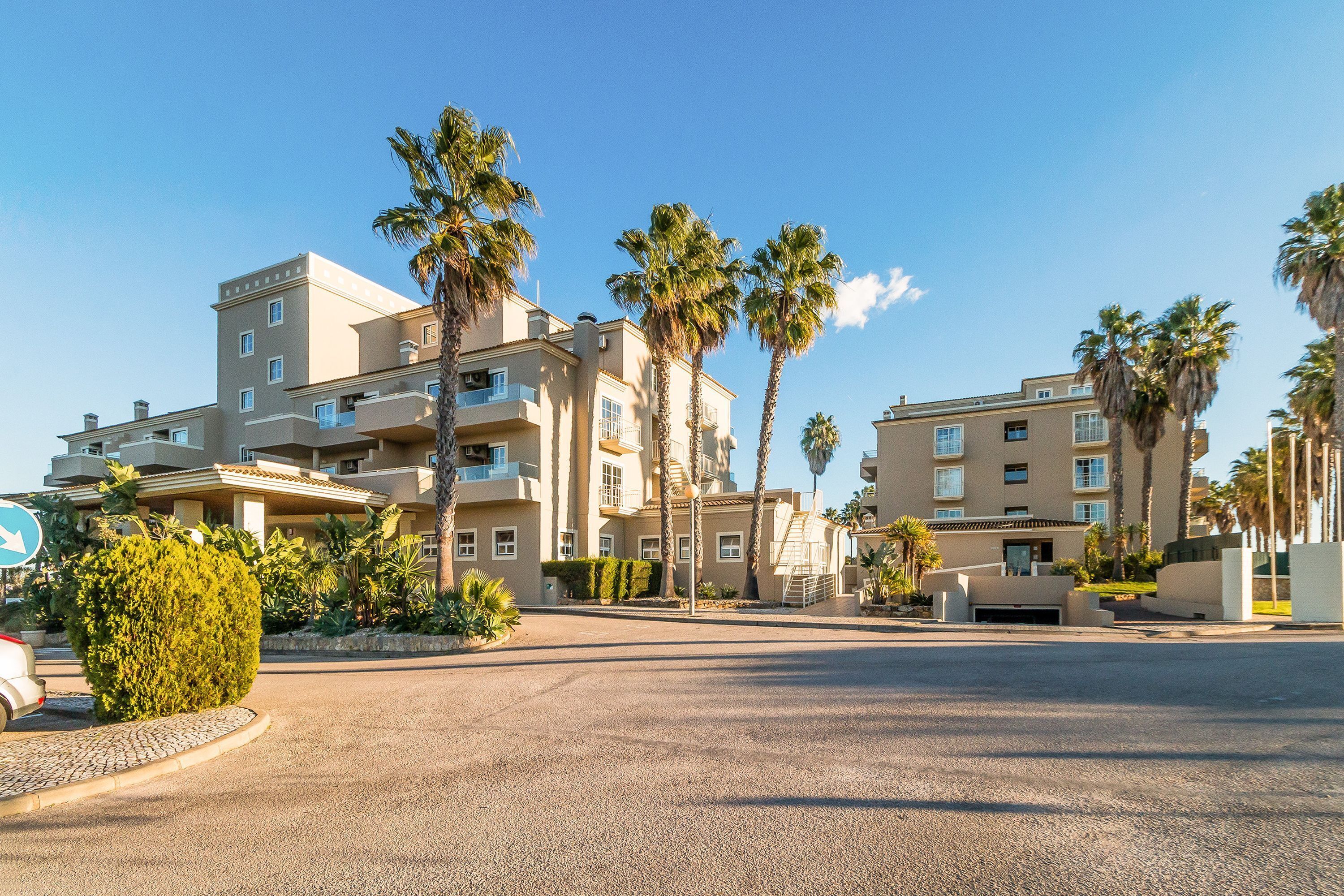 A multi-story hotel with balconies, palm trees, and a paved driveway.