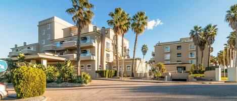 A multi-story hotel with balconies, palm trees, and a paved driveway.