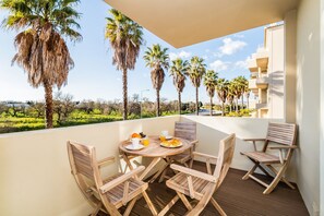 A balcony with a wooden table and chairs, a breakfast setting, and a view of palm trees and a building. - Portim o Resort Private Parking Pool (Portimão)