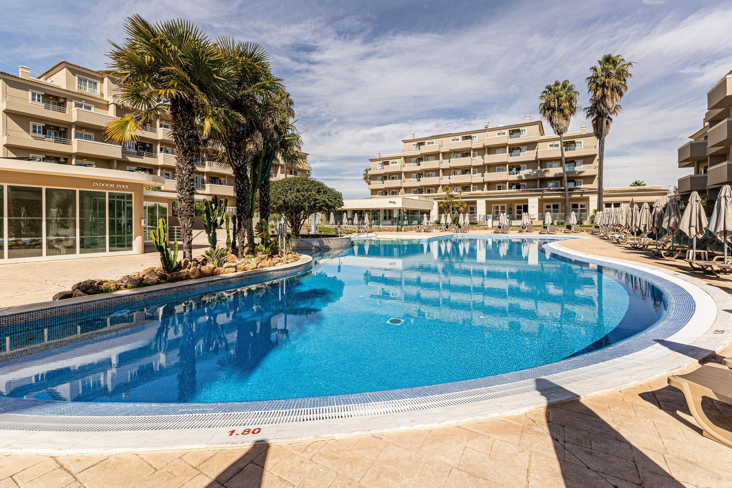 A swimming pool surrounded by palm trees and a multi-story hotel building.