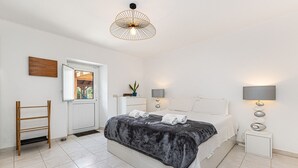 Un dormitorio con cama, mesitas de noche, lámpara colgante, ventana y puerta.