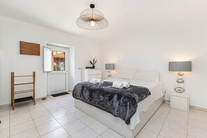 Une chambre à coucher comprenant un lit, des tables de chevet, un luminaire suspendu, une fenêtre et une porte.