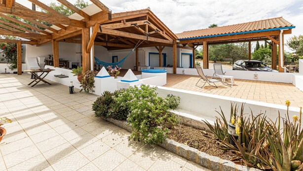 Un espacio al aire libre cubierto con una pérgola de madera, asientos y una piscina.
