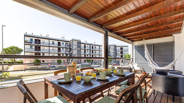Eine Terrasse im Freien mit einem Holztisch, gedeckt für ein Frühstück, einer Hängematte und Blick auf Wohnhäuser.
