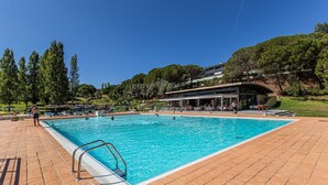 Ein Schwimmbad mit Fliesenbord, umgeben von Bäumen und einem Gebäude mit gewölbtem Dach.