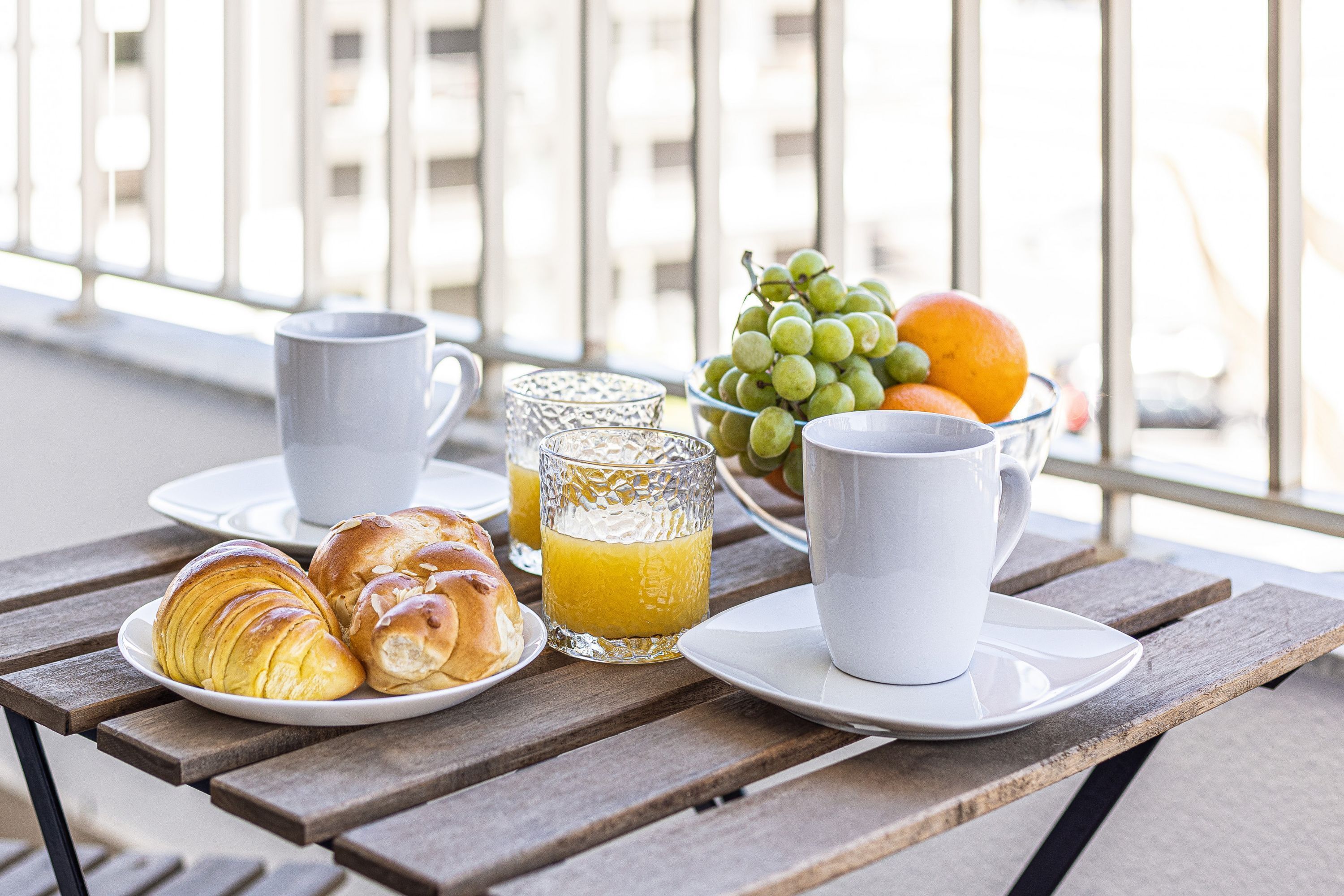 Ein Frühstückstisch mit Croissants, Orangensaft und einer Obstschale.