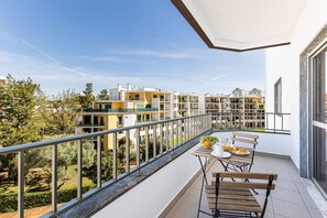 Een balkon met een ontbijtje, een hekwerk en uitzicht op moderne gebouwen en groen.