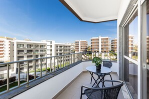 Een balkon met een tafel en stoelen, een plant in pot en uitzicht op omliggende gebouwen.