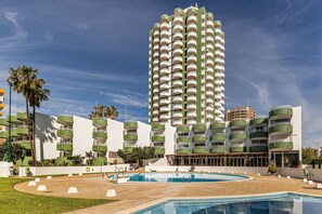 Ein Hochhaus-Hotel mit mehreren Balkonen, einem Schwimmbad und einem gepflegten Rasen.