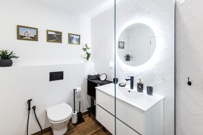A modern bathroom with a white sink, mirror, and toilet. There are framed pictures on the wall and a potted plant. - Torre Verde Sea View Apartments 906 (Portimão)