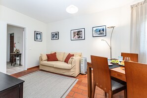 Ein Wohnzimmer mit Sofa, einem Esstisch mit Stühlen, einem Heizkörper und gerahmten Bildern an der Wand.