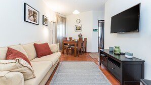 Ein Wohnzimmer mit einer Couch, einem Esstisch, Stühlen, einem Flachbildfernseher und einer Wanduhr.