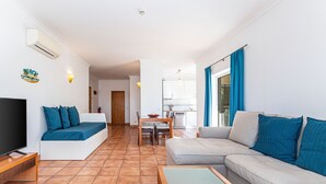 A living room with a TV, sofa, and coffee table, a dining area with chairs and a table, and a kitchen in the background. - Porto de Mos - Nucleo 2 (Lagos)
