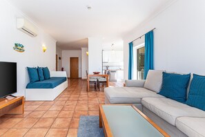 A living room with a TV, sofa, and coffee table, a dining area with chairs and a table, and a kitchen in the background. - Porto de Mos - Nucleo 2 (Lagos)