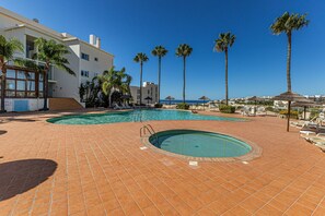 Área de piscina com duas piscinas, palmeiras e um edifício com varandas.