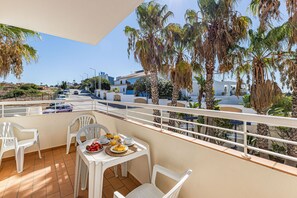 Uma varanda com mesa posta para o café da manhã, cadeiras brancas e vista para a rua e edifícios.