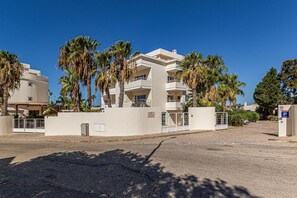Ein mehrstöckiges Hotel mit Balkonen, Palmen und einem Parkplatz.