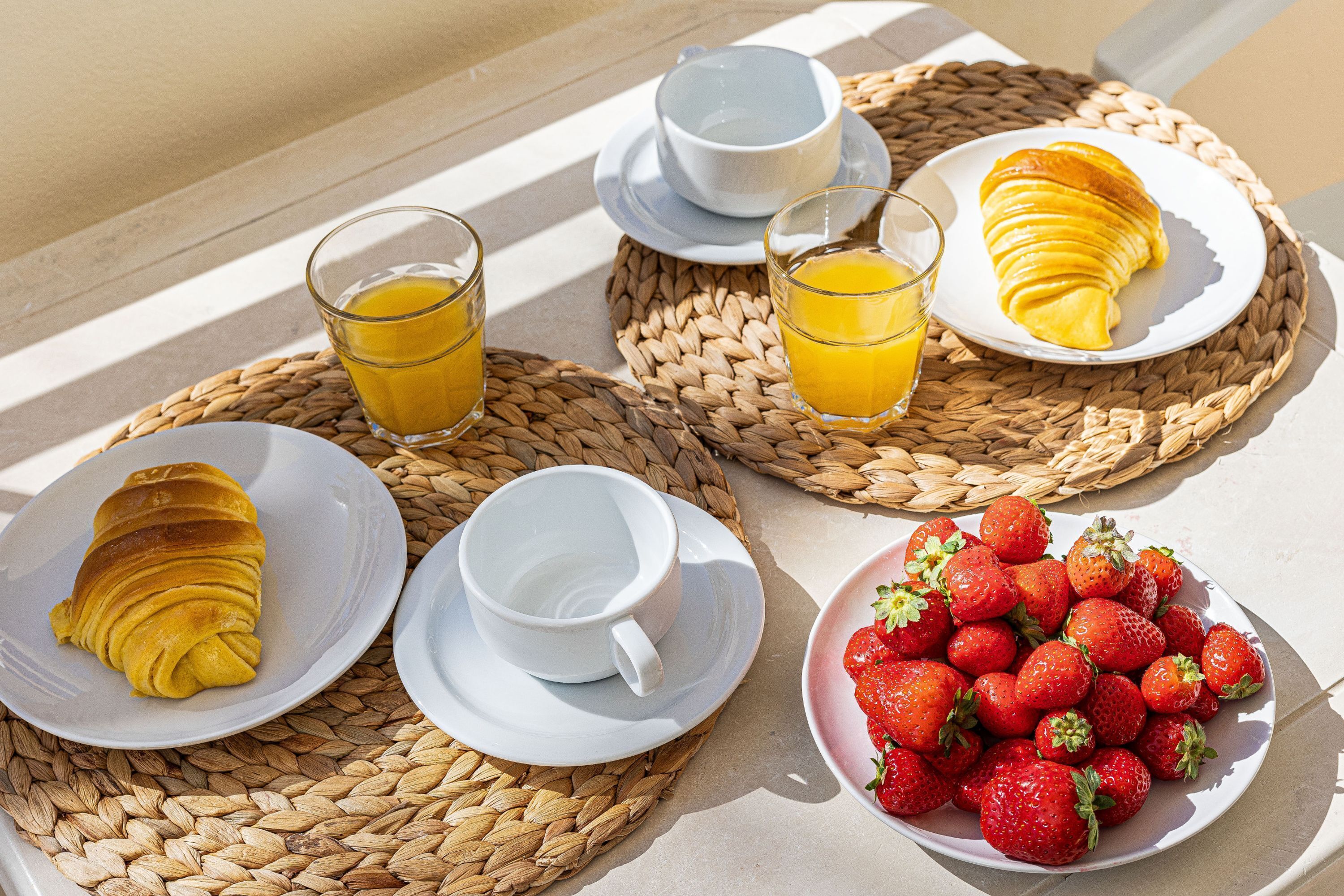 Un plateau de petit-déjeuner avec des croissants, du jus d’orange et des fraises, le tout disposé sur des sets de table en fibres tressées.