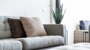 Ein graues Sofa mit zwei Kissen, einer Topfpflanze und einem kleinen Tisch mit einem Stuhl.