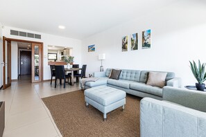 Uma sala moderna com um sofá seccional, uma área de refeições e uma cozinha ao fundo.