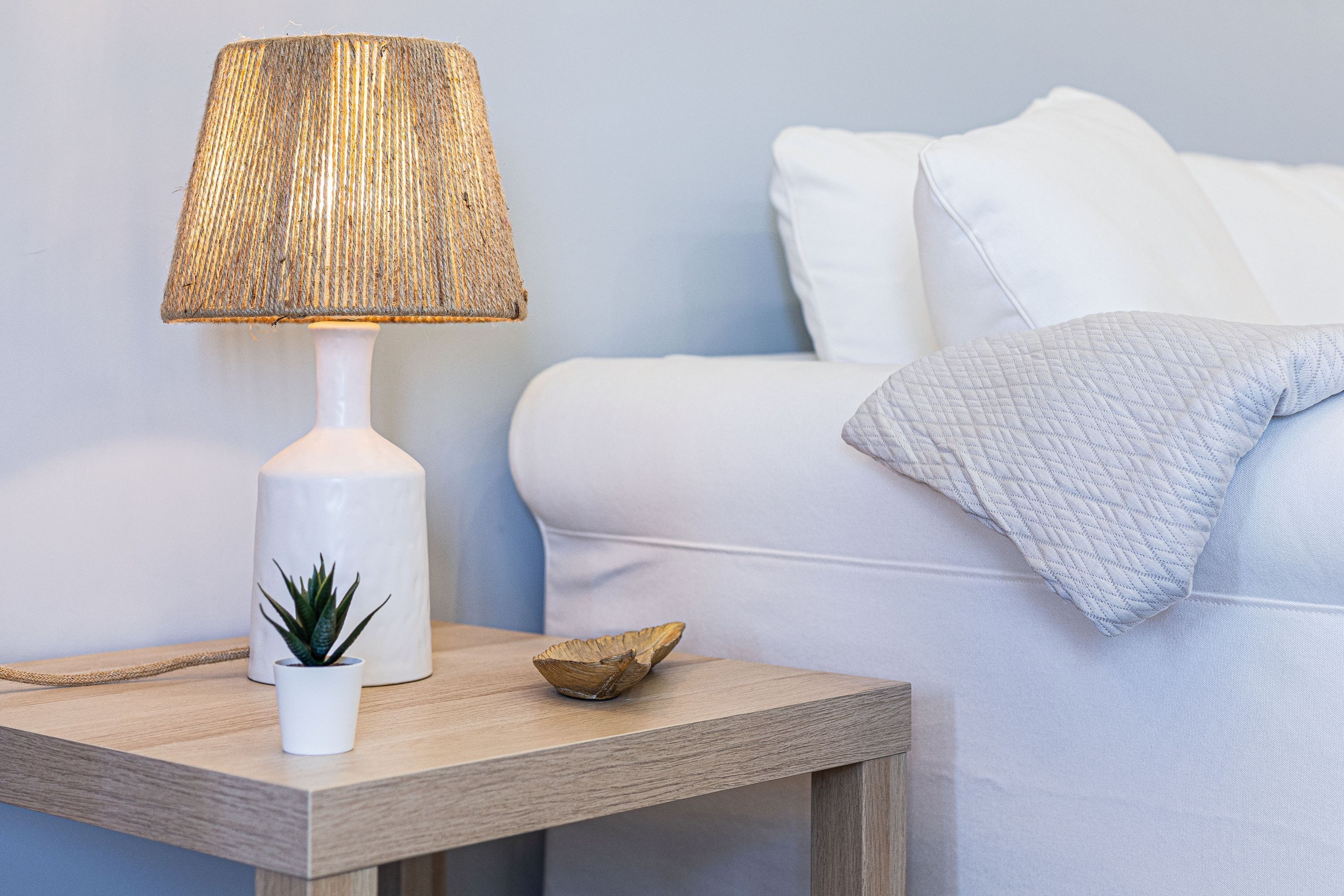 Een nachtkastje met een lamp, een kleine potplant en een decoratieve schaal.