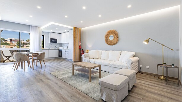 Una sala de estar moderna con sofá, reposapiés, mesa de centro y un comedor con sillas.