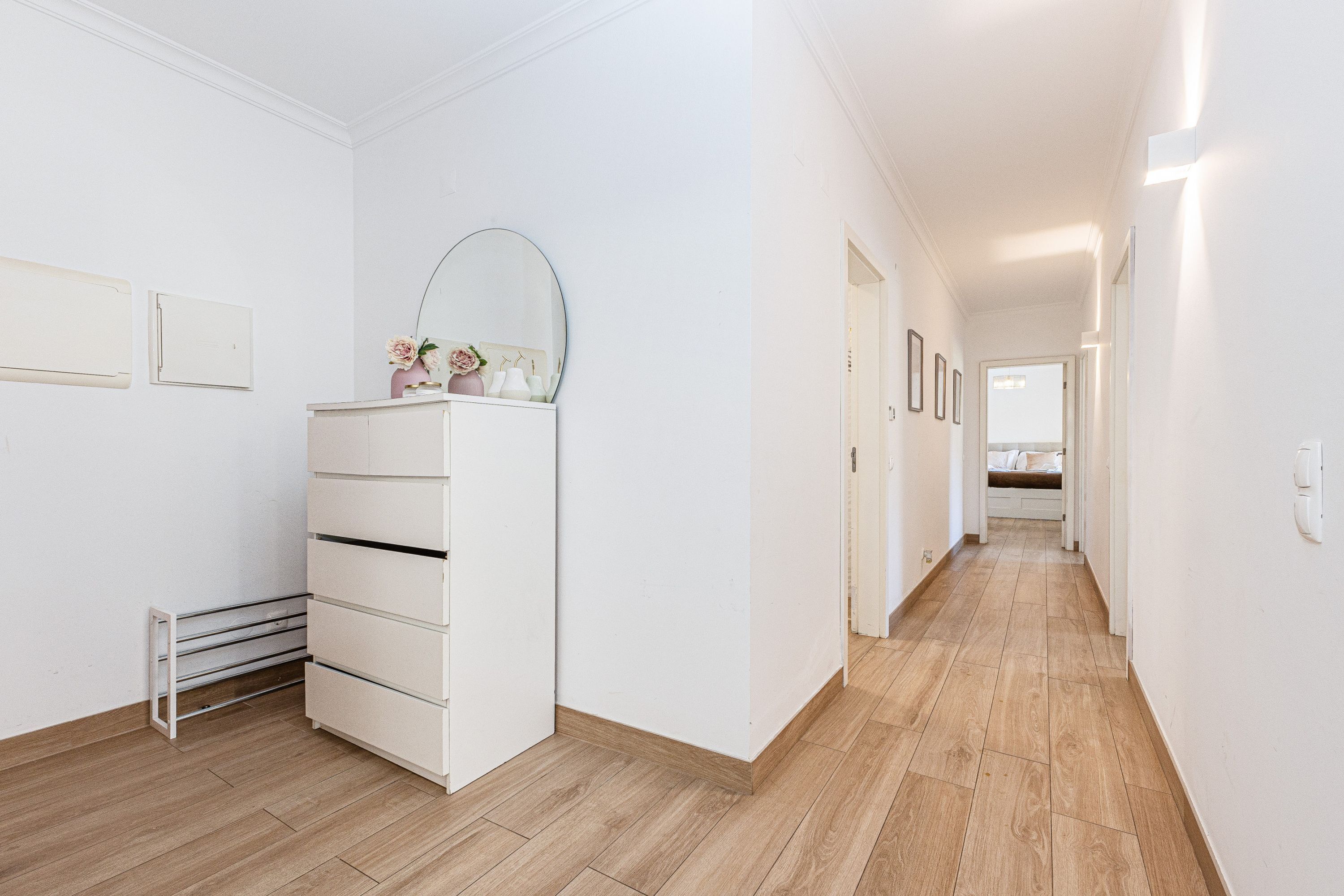 Un couloir avec une commode blanche, un miroir et des tableaux encadrés accrochés au mur.
