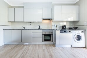 Eine moderne Küche mit weißen Schränken, einem eingebauten Ofen, einer Waschmaschine und einer Arbeitsplatte aus Granit.