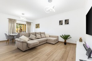Ein modernes Wohnzimmer mit einer Eckcouch, einem Esstisch mit Stühlen, einem Topf mit Pflanze und Kunstwerken an den Wänden.