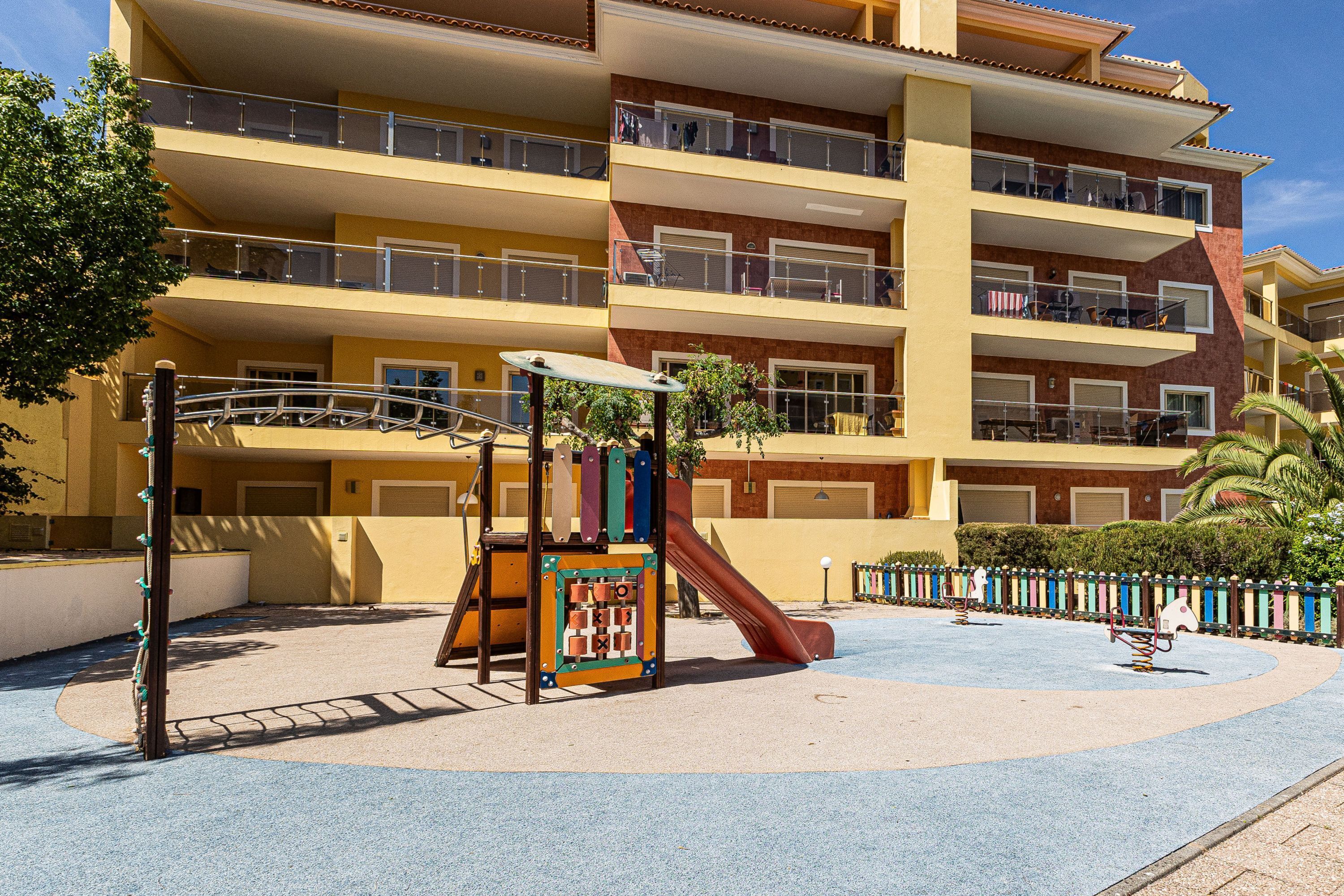 A multi-story building with balconies, a playground with a slide, and a pool area.