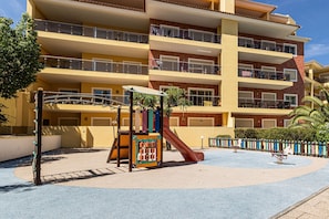 Ein mehrstöckiges Gebäude mit Balkonen, einem Spielplatz mit Rutsche und einem Poolbereich.