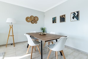 Ein Essbereich mit einem Holztisch, weißen Stühlen, einer Stehlampe und Wandbildern.