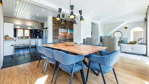 A modern kitchen with a central island, a dining area with blue chairs, and a living room with a grey sofa. - Casa Corsino in Marmelete (Monchique)